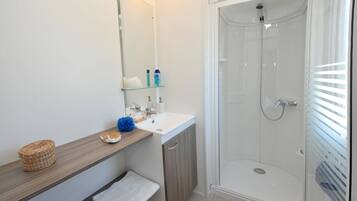 Un baño moderno con ducha de vidrio, un lavabo blanco y un espejo encima.