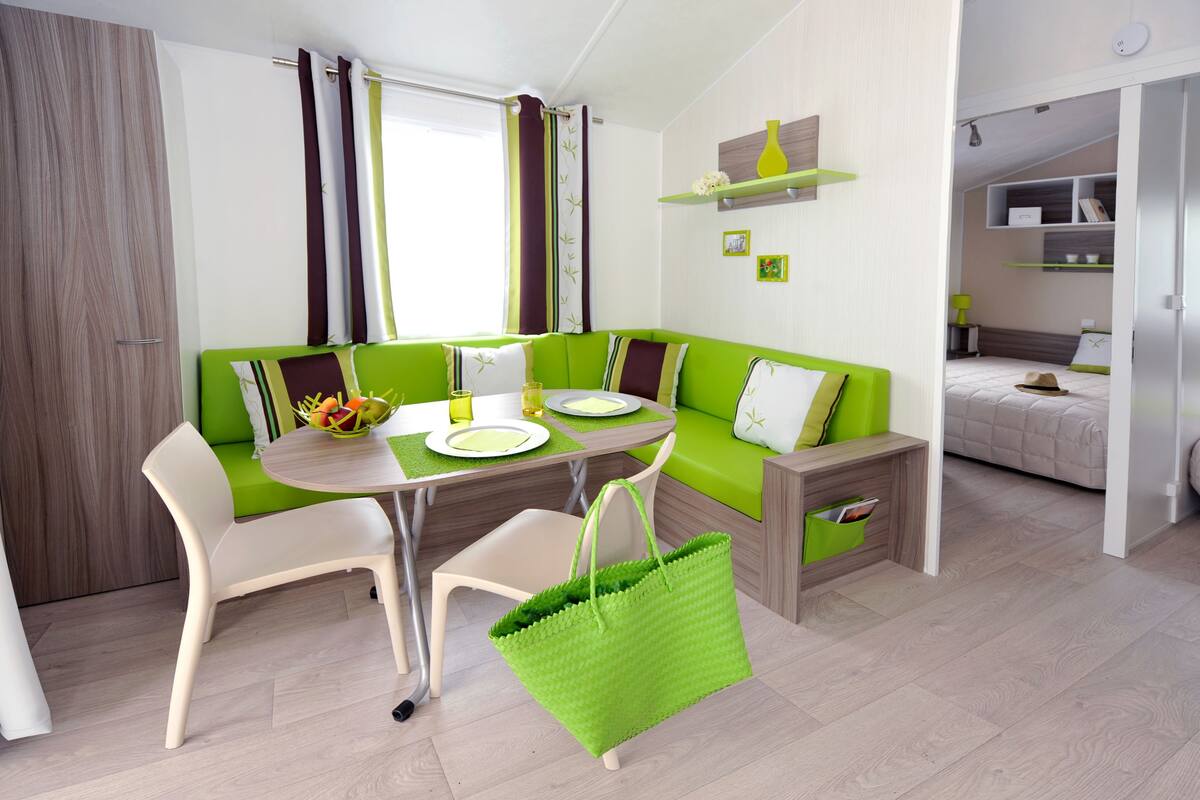 Une pièce moderne et bien éclairée, avec un canapé vert, une table à manger et un sac vert posé sur le sol.