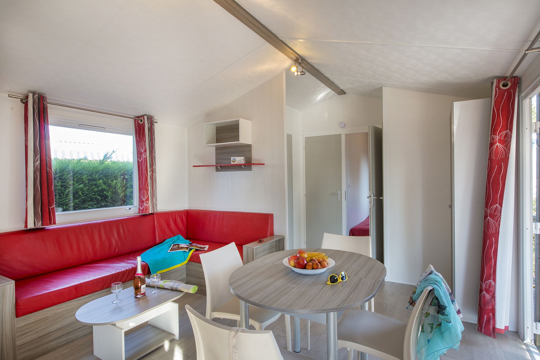 A modern room with a red sofa, a small table with a bowl of fruit, and a window with curtains.