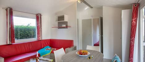 A modern room with a red sofa, a small table with a bowl of fruit, and a window with curtains.