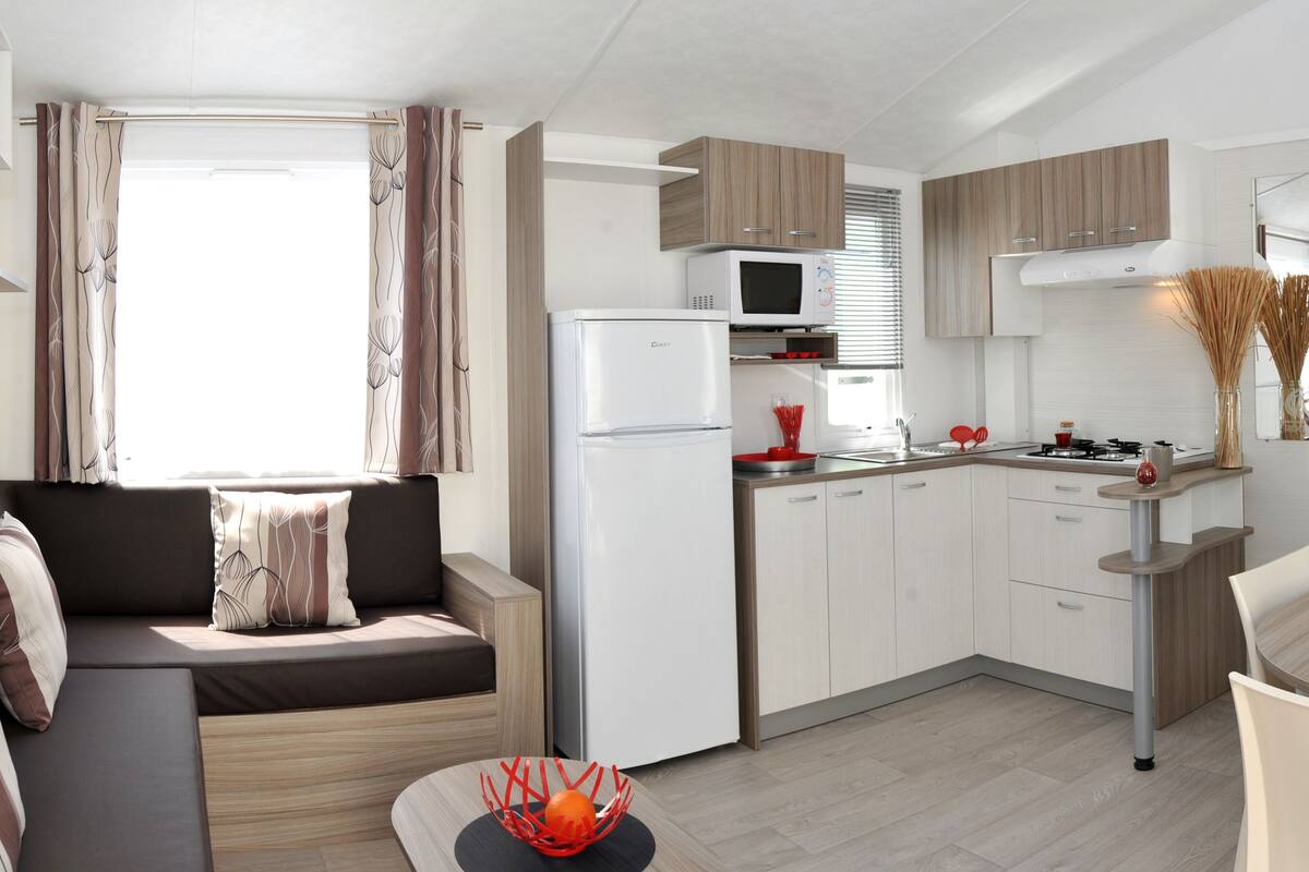 Une cuisine compacte équipée d’un four à micro-ondes, d’une cuisinière et d’un évier. On y trouve une table à manger avec des chaises, ainsi qu’un canapé avec des coussins.
