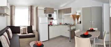 A compact kitchen with a microwave, stove, and sink. There is a dining table with chairs and a sofa with cushions.