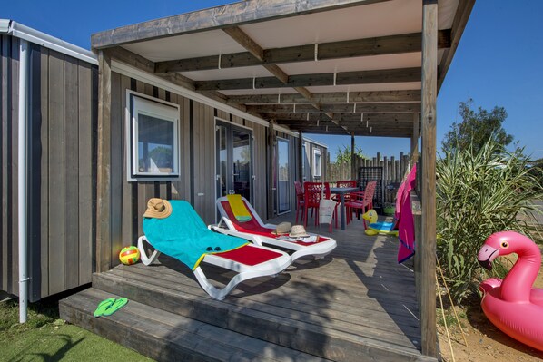 A covered outdoor area with wooden deck, two sun loungers, a pink flamingo float, and a patio table with chairs.