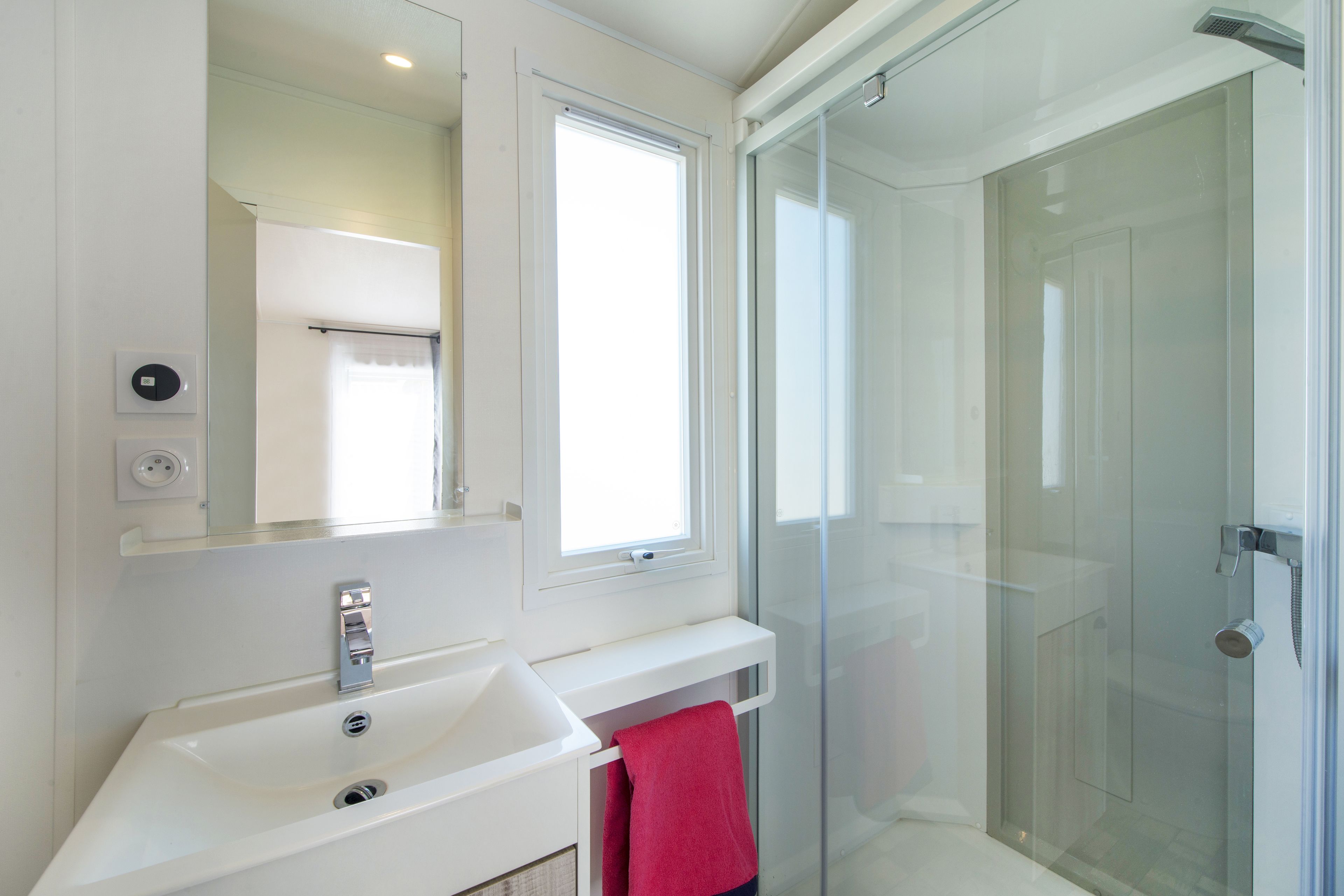 Un bagno moderno con un lavandino bianco, uno specchio, cabina doccia in vetro e un asciugamano rosso.