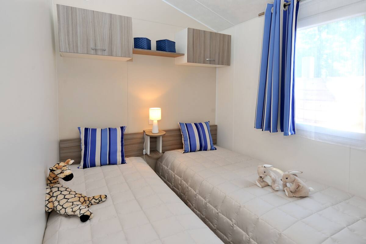 Une chambre avec deux lits, une table de chevet, une lampe et deux peluches.