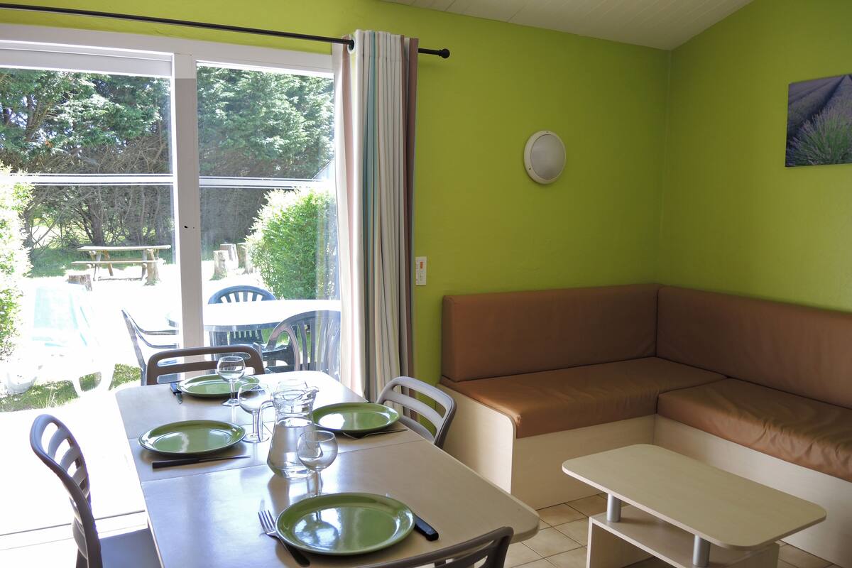 Un coin repas avec une table dressée pour quatre personnes, un canapé et un petit banc.