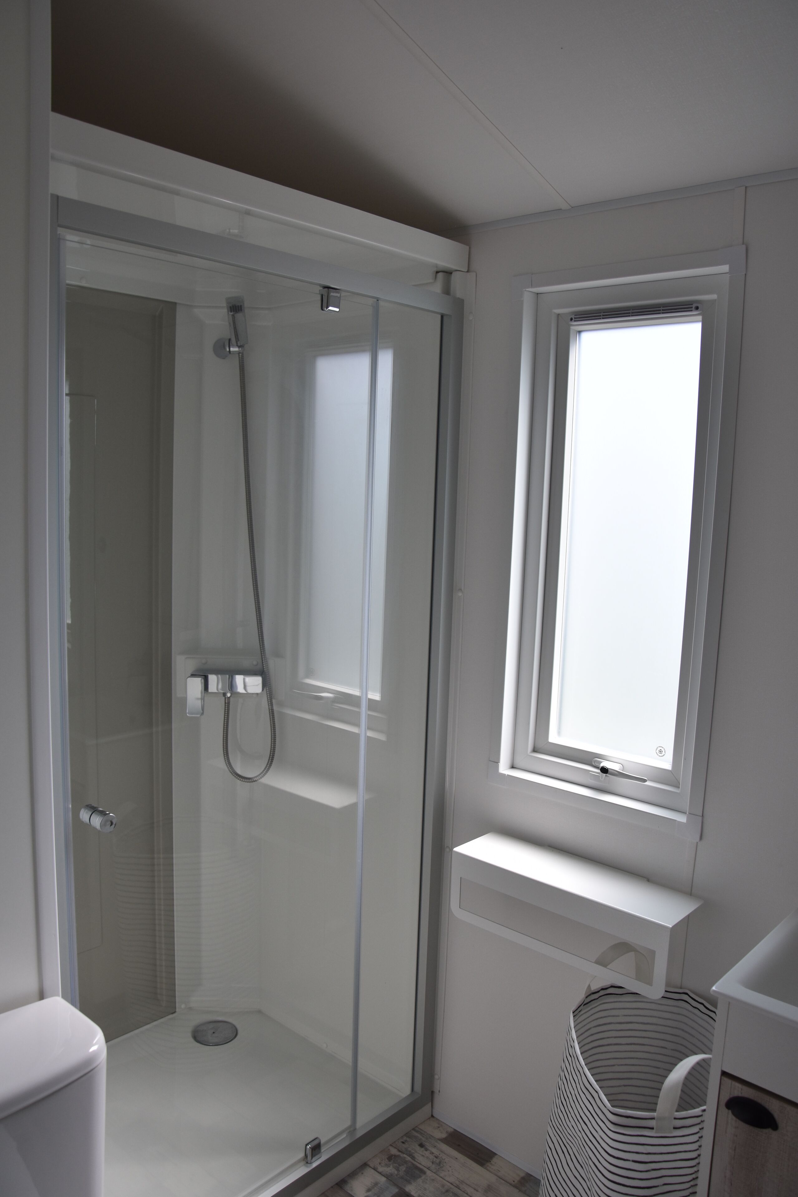 Une salle de bain moderne avec une douche à parois de verre, une fenêtre et un lavabo blanc.