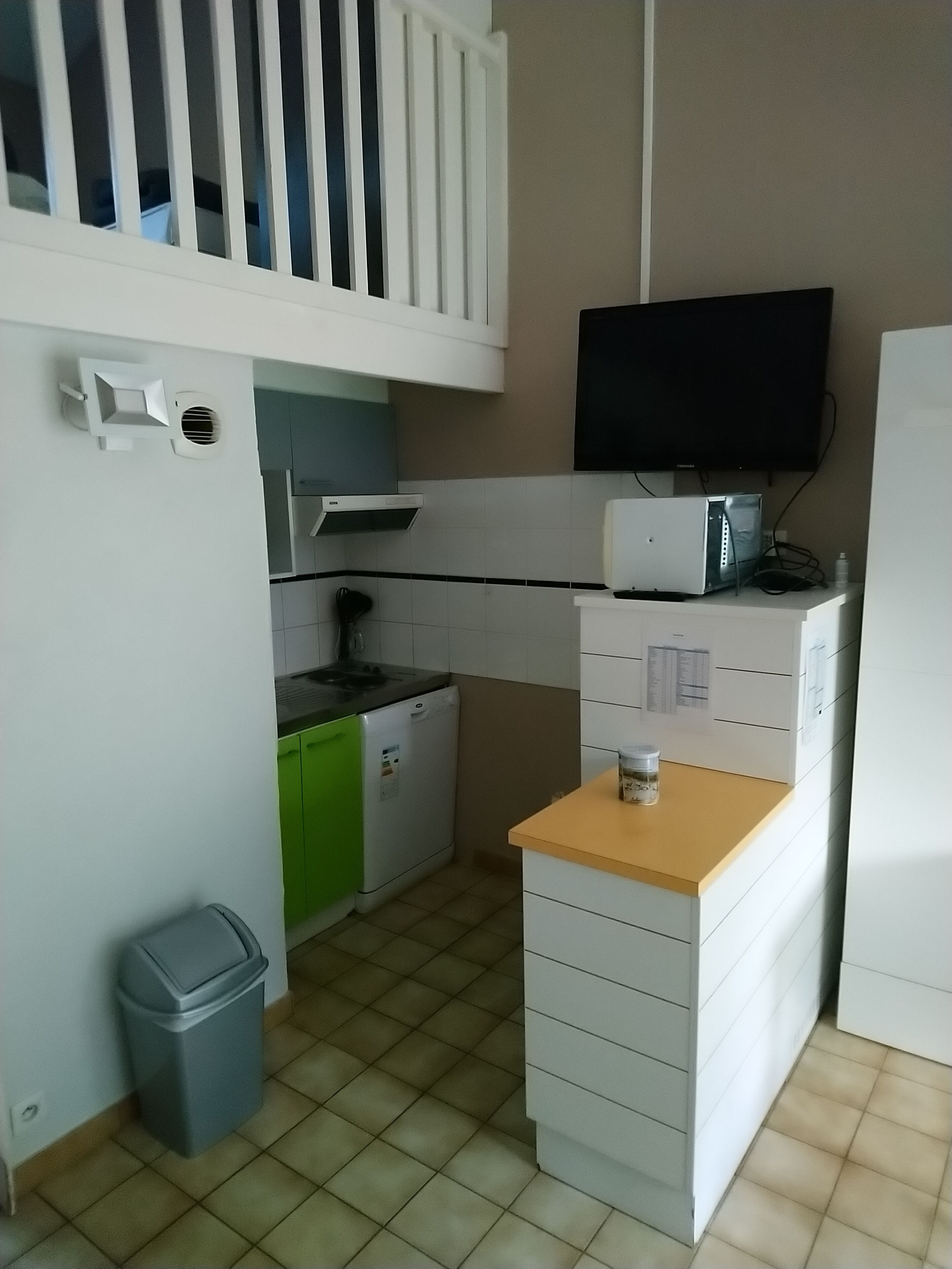 Een kleine keuken met een magnetron, een kleine koelkast, een spoelbak en een vuilnisbak.