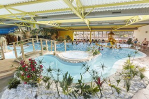 Een binnenzwembad met een jacuzzi, omringd door planten en een houten terras.