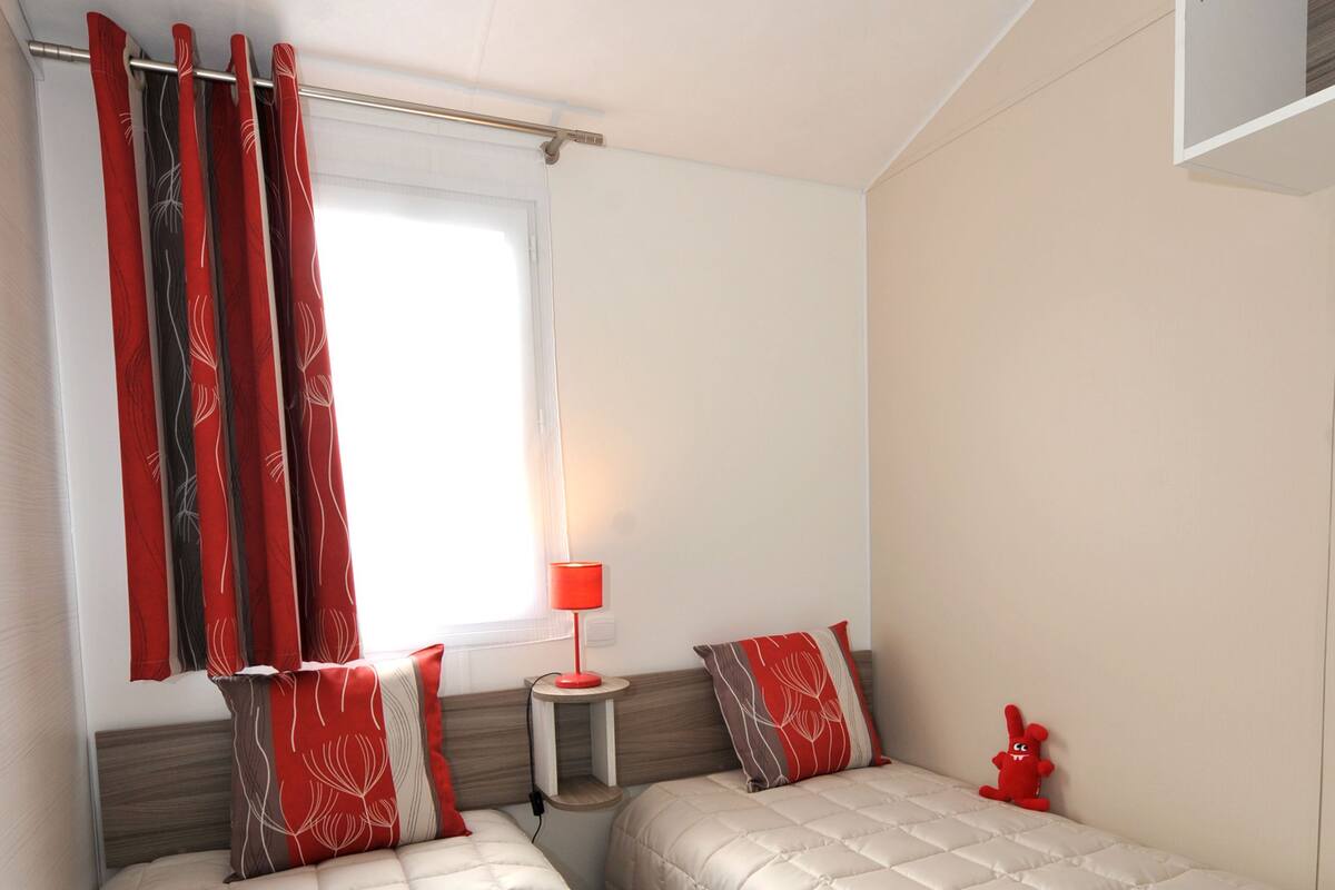 Une chambre avec deux lits, une table de chevet, une lampe et une fenêtre avec des rideaux.