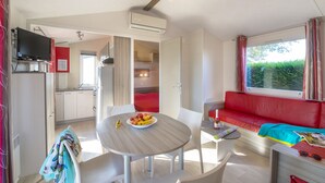Een moderne, goed verlichte kamer met een eettafel, stoelen, een rode bank en een televisie.
