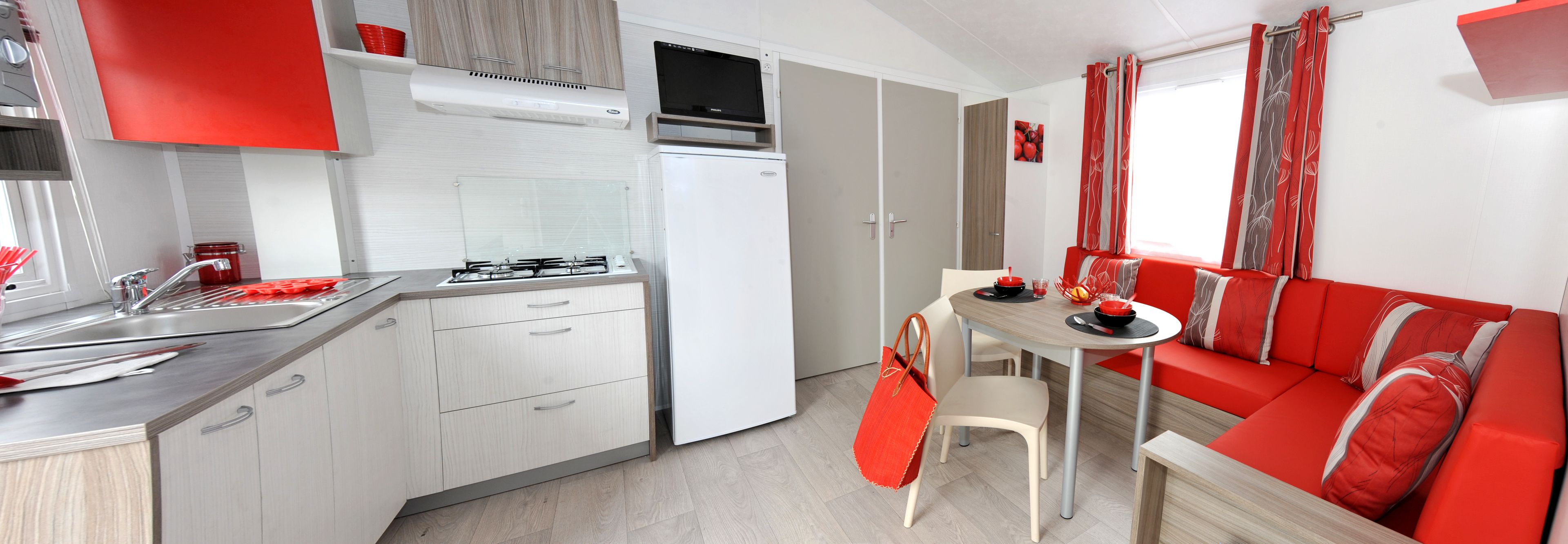 A compact kitchen with a stove, sink, and cabinets, a dining area with a table and chairs, and a red sofa.
