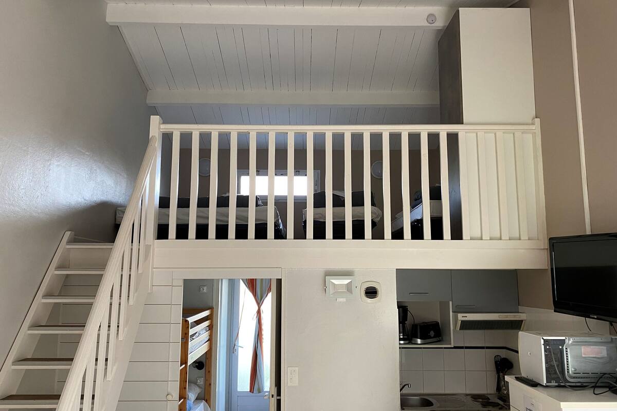 Un appartement compact avec une chambre en mezzanine, une kitchenette et un escalier.
