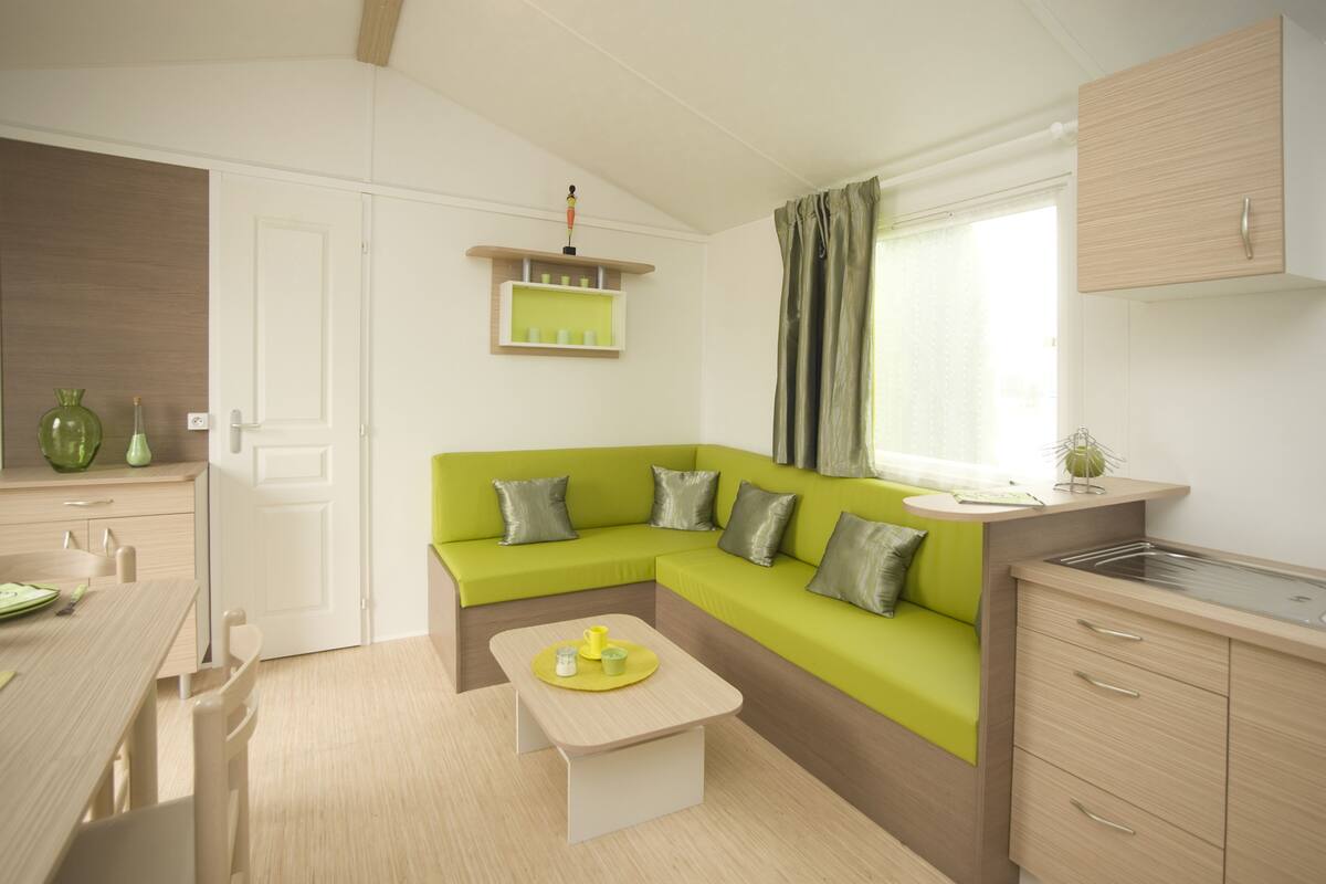 Un espace de vie compact et moderne, avec un canapé vert, une petite table à manger et un coin cuisine.