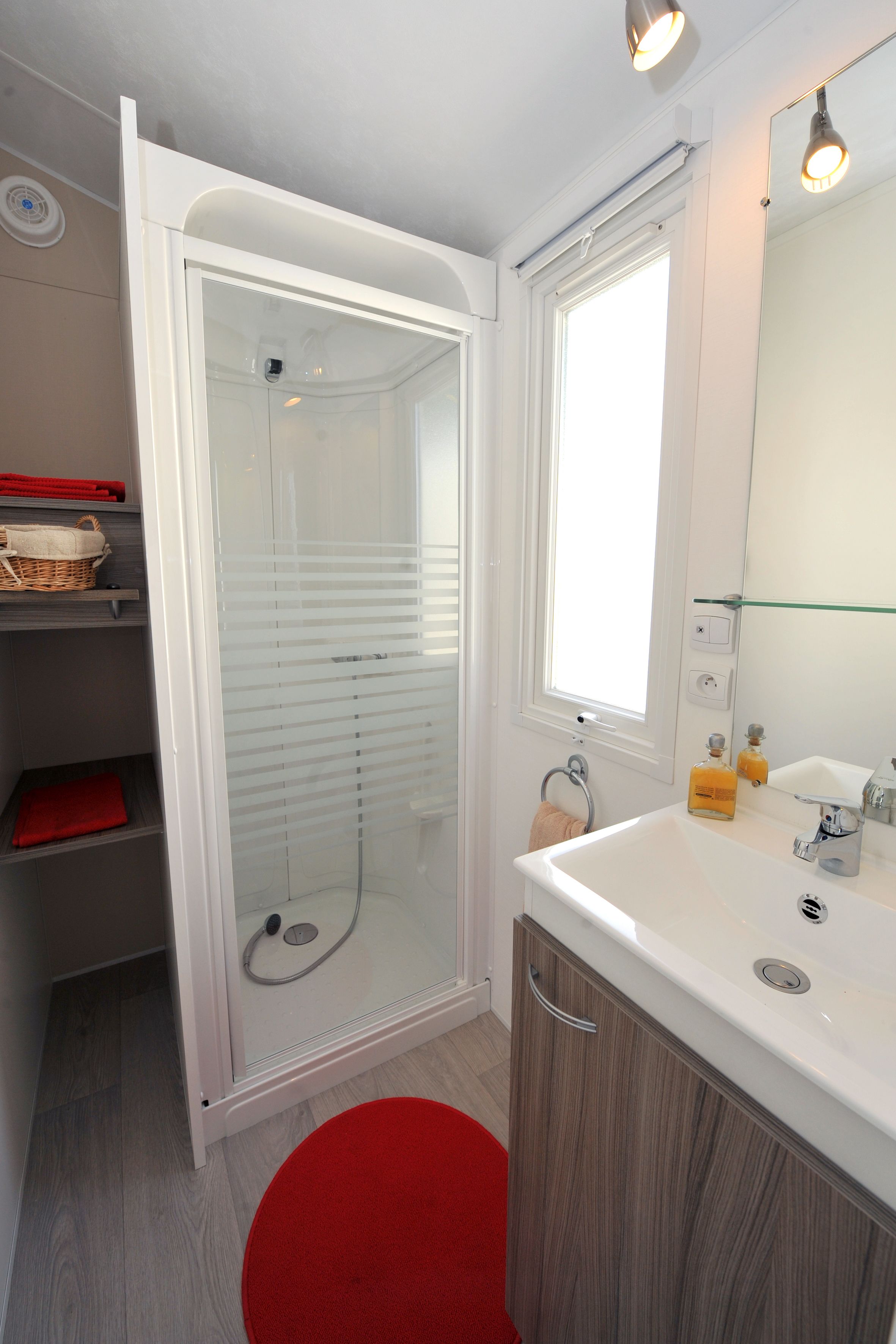 Un baño moderno con ducha de vidrio, un lavabo blanco con espejo y un tapete rojo.