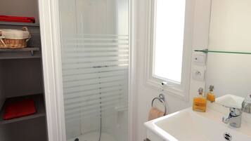 Un baño moderno con ducha de vidrio, un lavabo blanco con espejo y un tapete rojo.