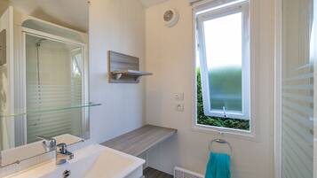 Een badkamer met een glazen douchecabine, een witte wastafel en een raam met uitzicht op groen.