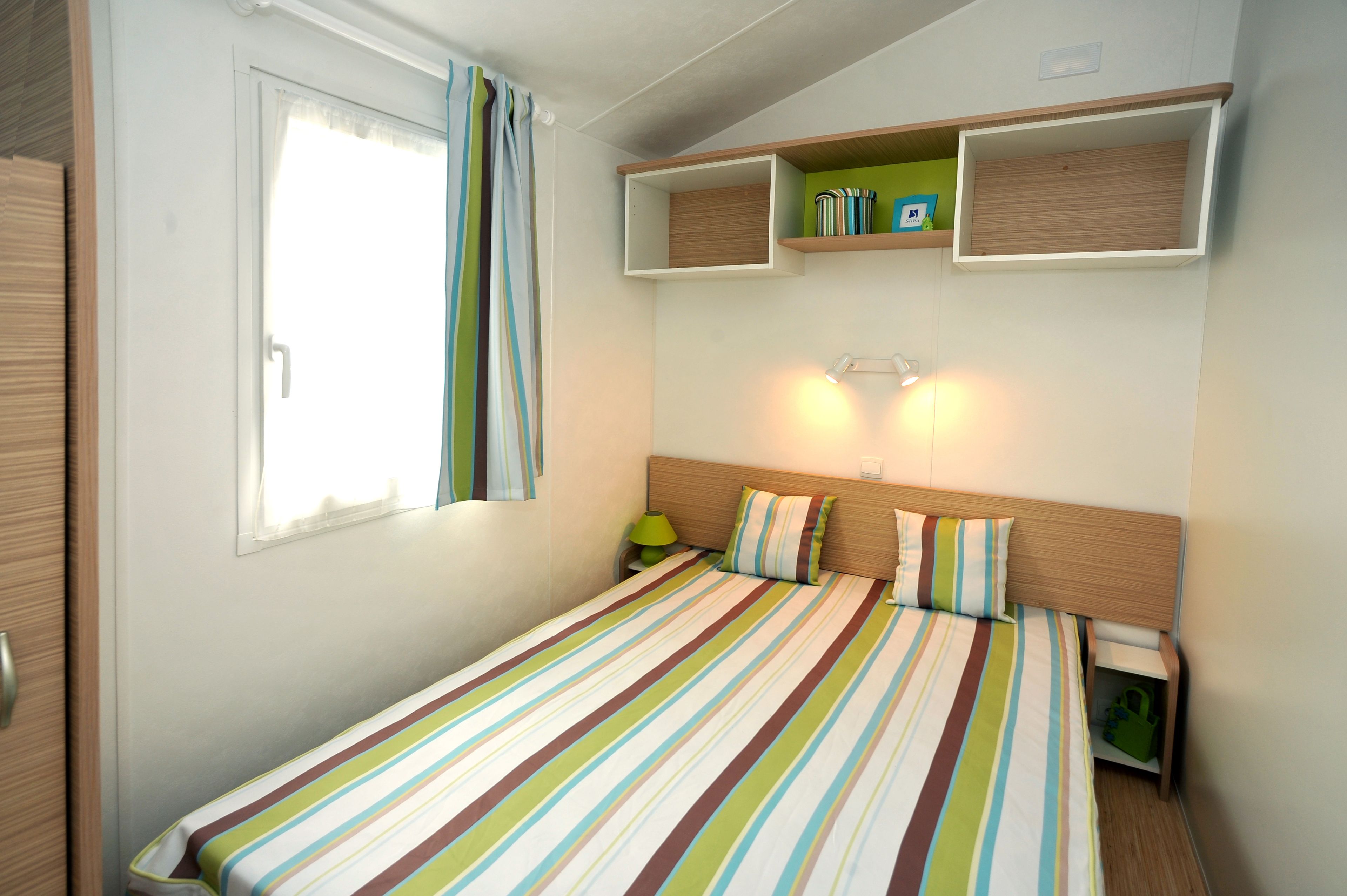 A single bed with striped bedding, a nightstand with a lamp, and built-in shelving above the bed.