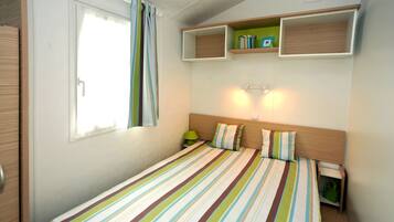 A single bed with striped bedding, a nightstand with a lamp, and built-in shelving above the bed.