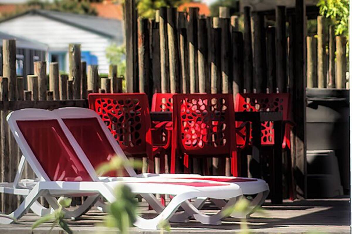 Deux chaises longues blanches avec des coussins rouges, une clôture en bois et des panneaux décoratifs rouges en arrière-plan.