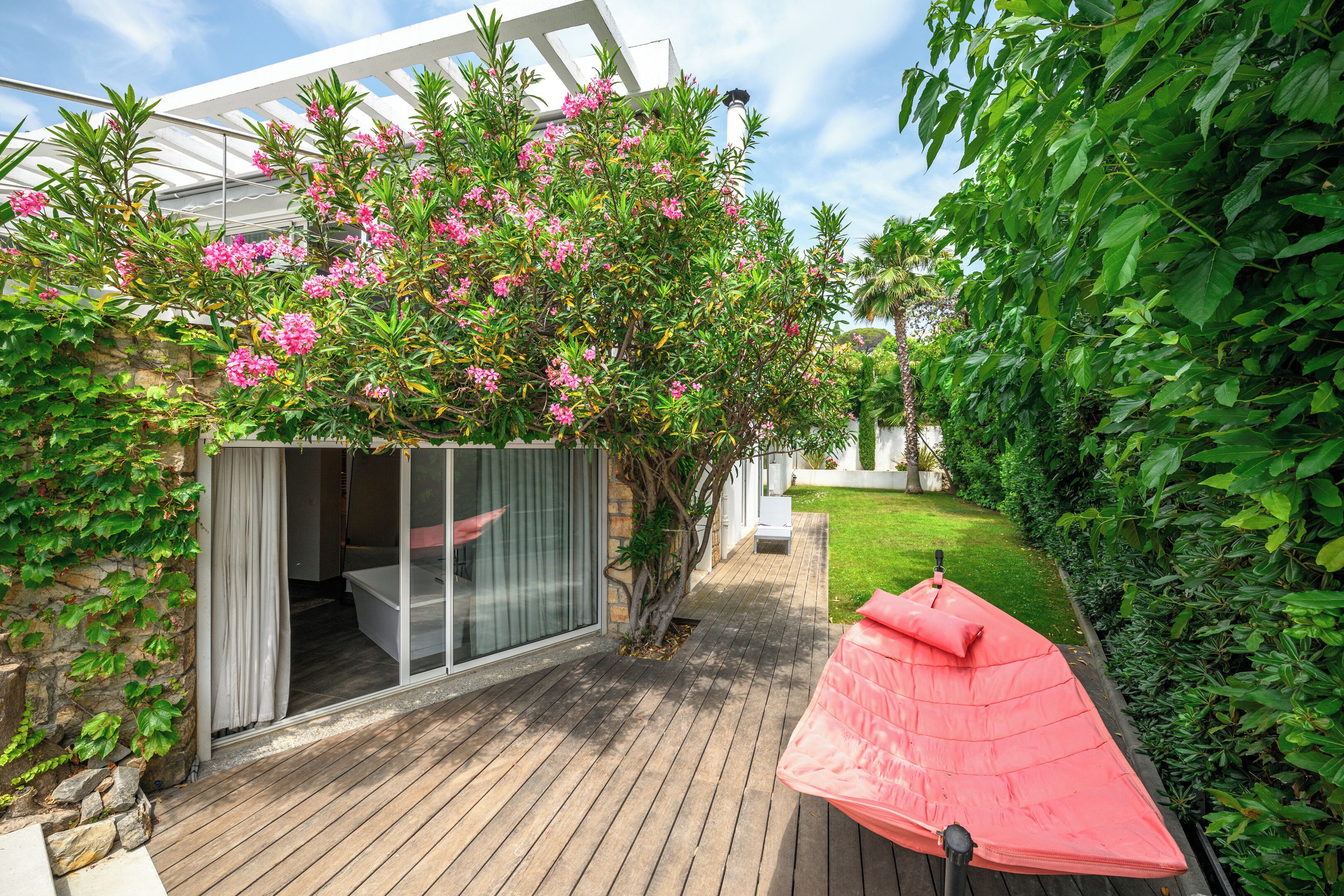 A wooden deck with a glass enclosure, a pink umbrella, and lush greenery.