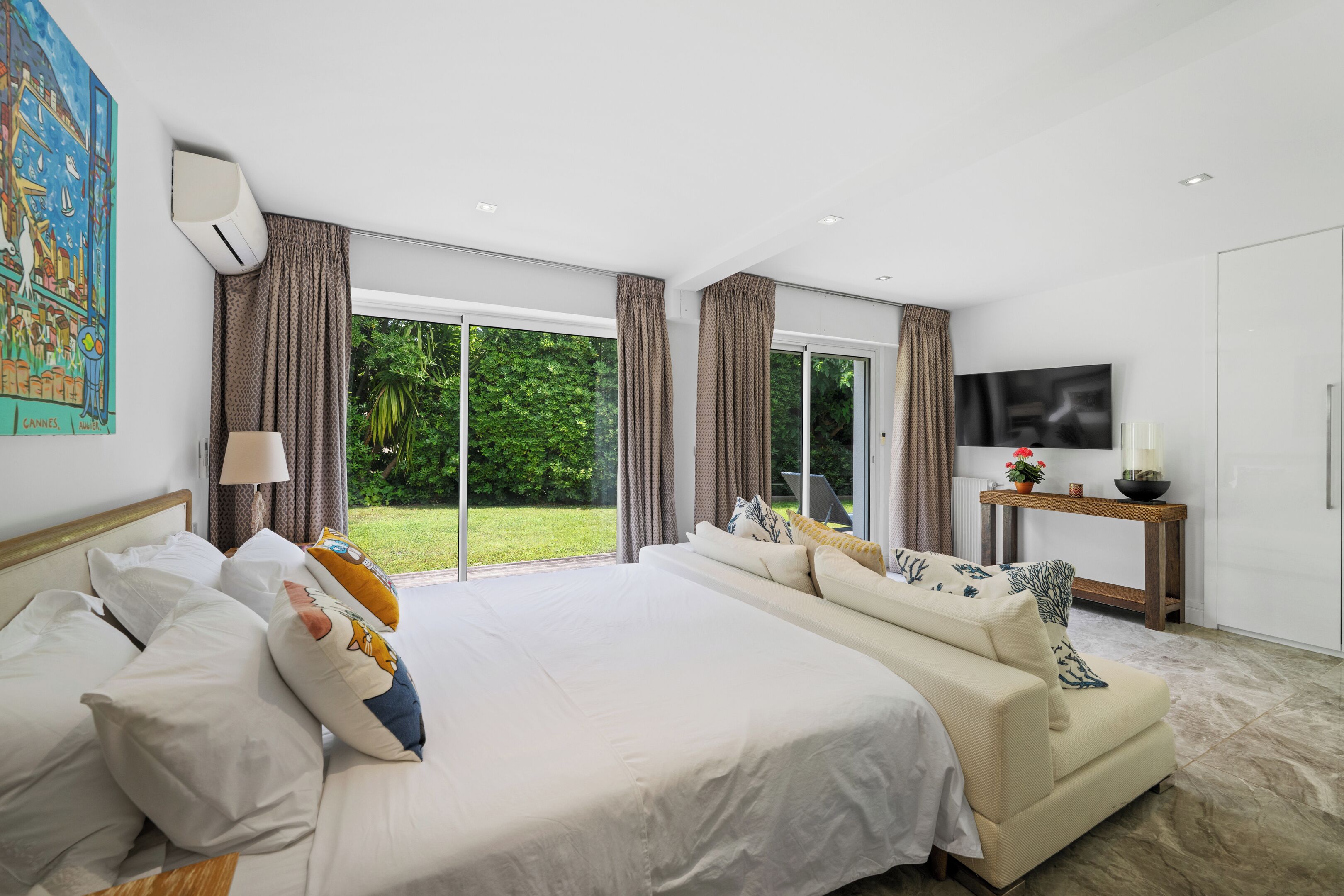 A modern hotel room with a large bed, a sofa, a TV, and a view of the outdoors.