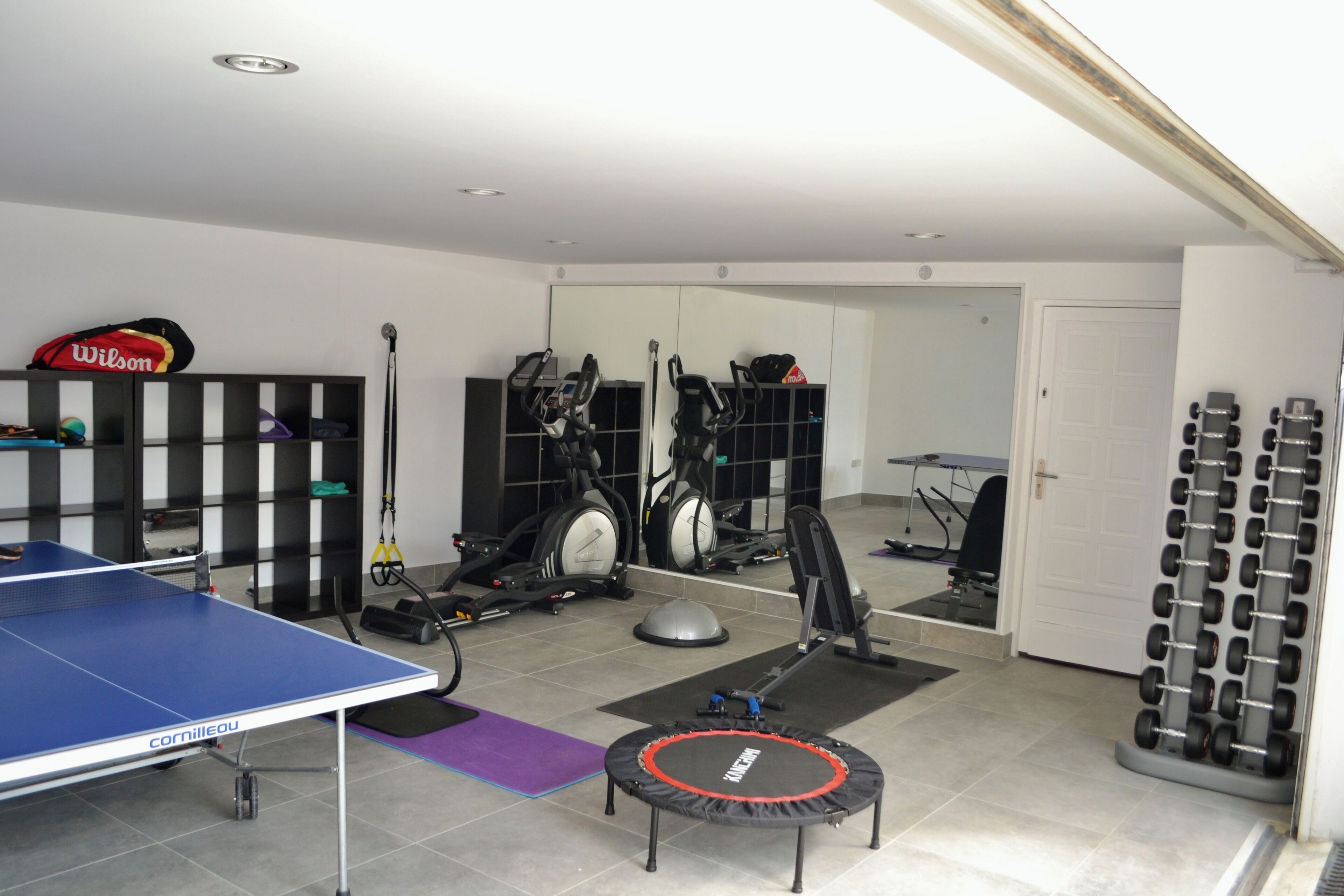 A gym with exercise equipment, a ping pong table, and a trampoline.