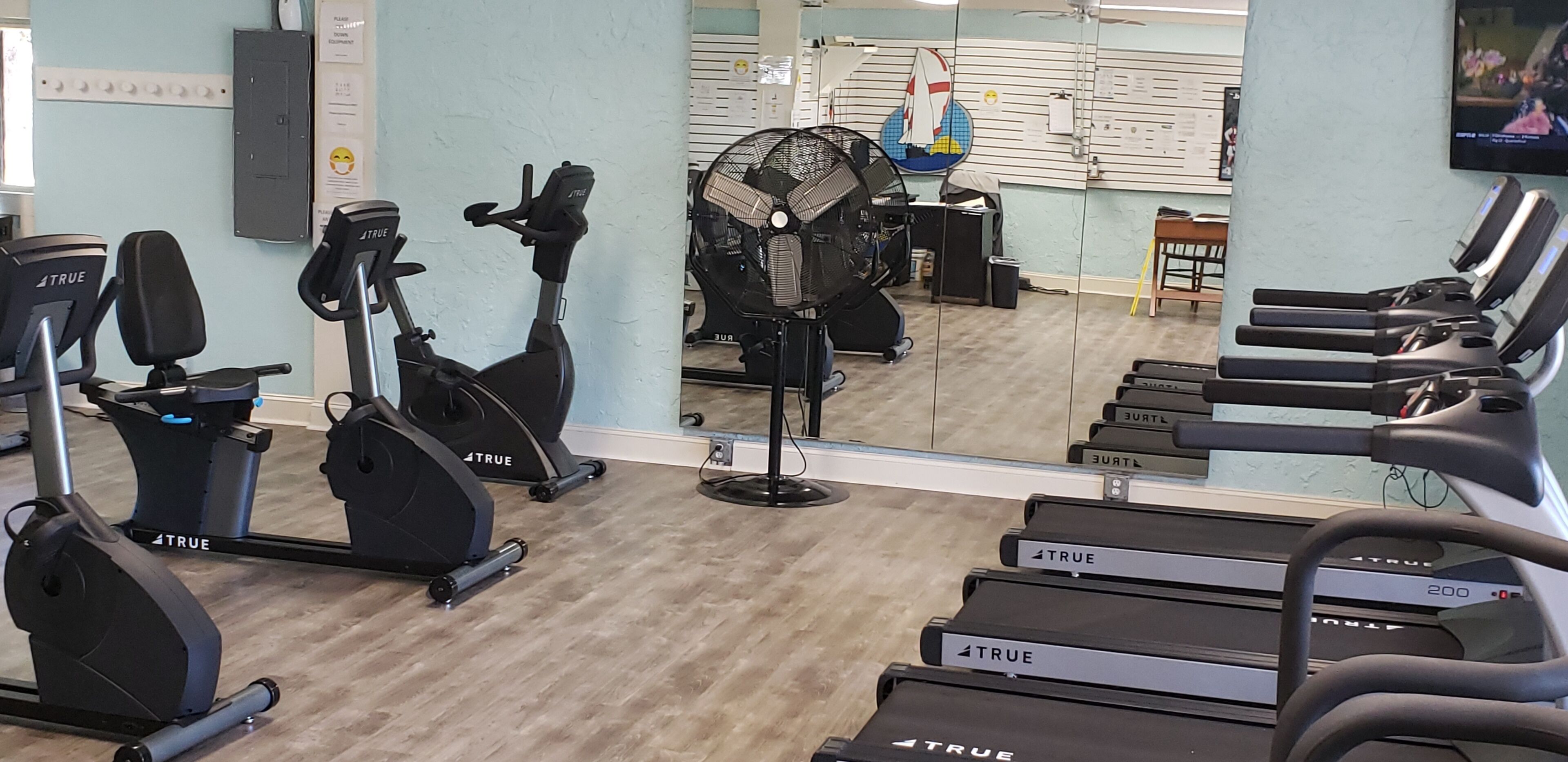 A gym with multiple exercise machines, including treadmills and stationary bikes, and a mirrored wall reflecting the room.