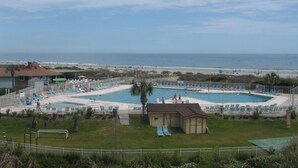 Un espace piscine comprenant plusieurs piscines, des chaises longues et un petit bâtiment, le tout offrant une vue sur la plage.