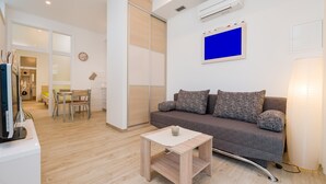 A modern living room with a grey sofa, a small wooden coffee table, and a TV on a white stand.