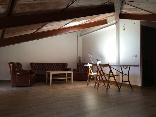 A room with a wooden ceiling, a brown leather sofa, a wooden table, and a chair with a white lamp.