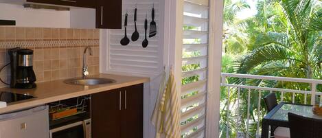 A kitchen with a sink, stove, and cabinets, and a balcony with a view of palm trees.