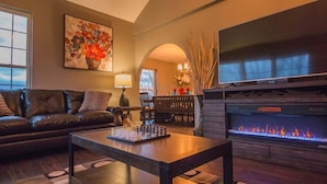 Una sala de estar con chimenea, un sofá, una mesa de centro con ajedrez y un televisor.