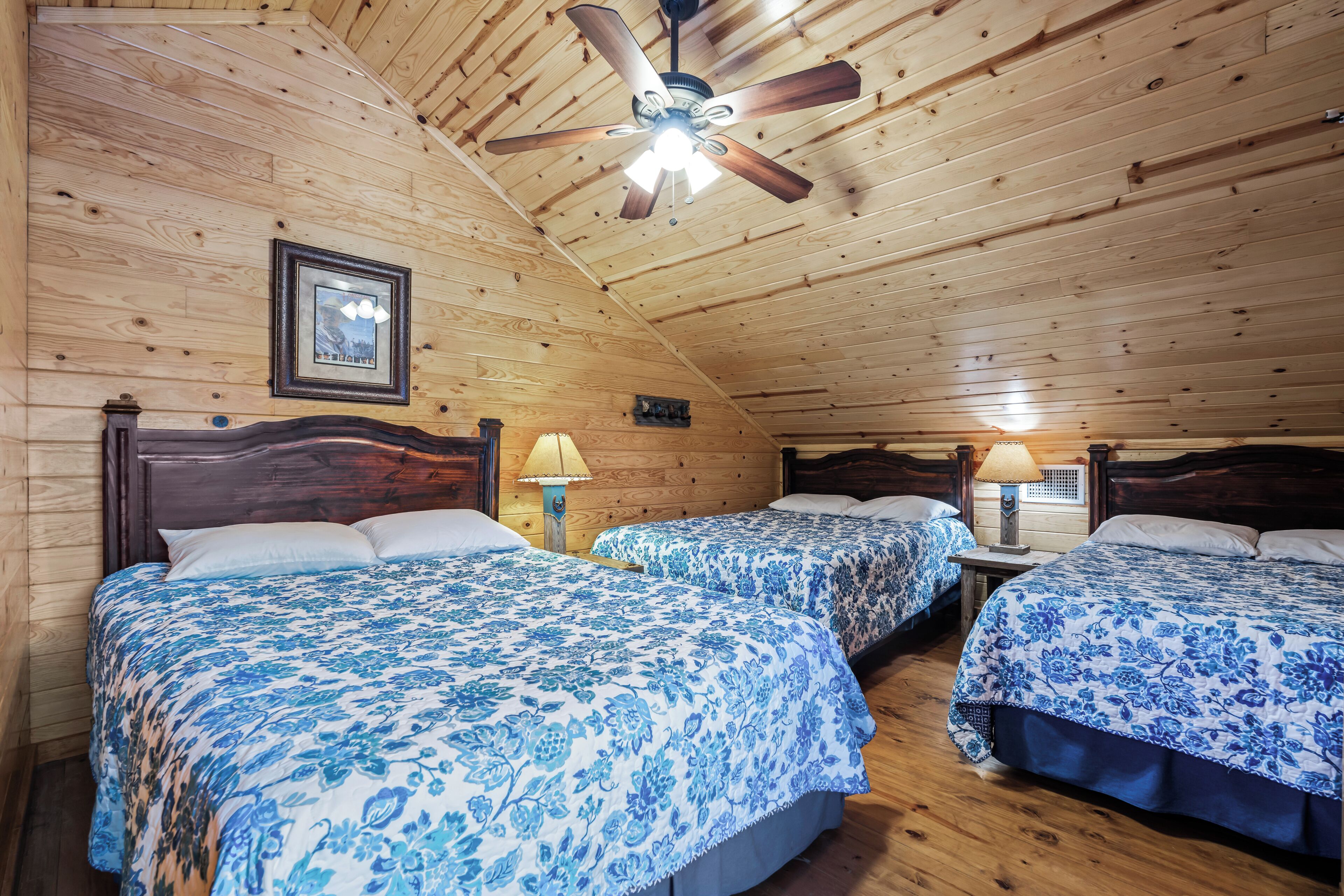 Ein Schlafzimmer einer Holzhütte mit zwei Betten, einem Deckenventilator und gerahmten Bildern an den Wänden.