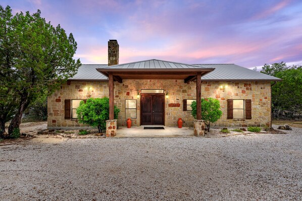 A stone house with a metal roof, a front porch, and a gravel driveway.