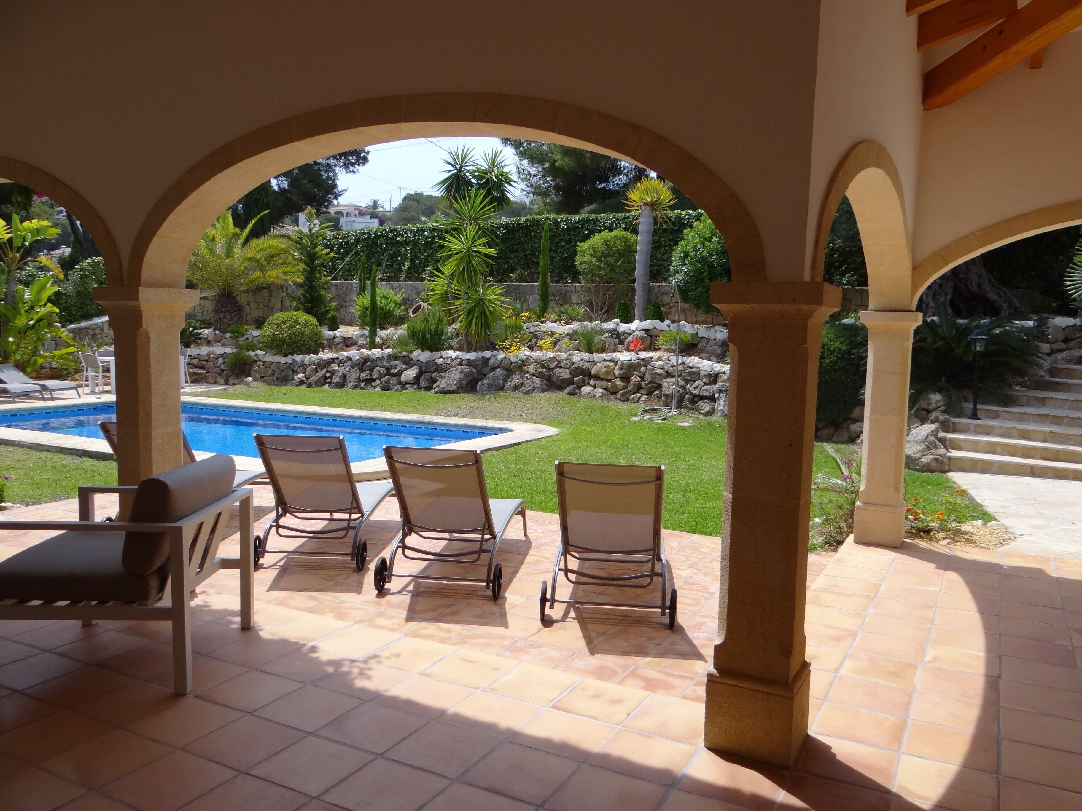 A covered patio area with a pool, outdoor seating, and a view of a landscaped garden.
