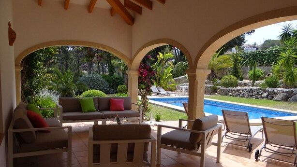 Eine überdachte Terrasse mit Pool, Gartenmöbeln und Blick auf den Poolbereich.