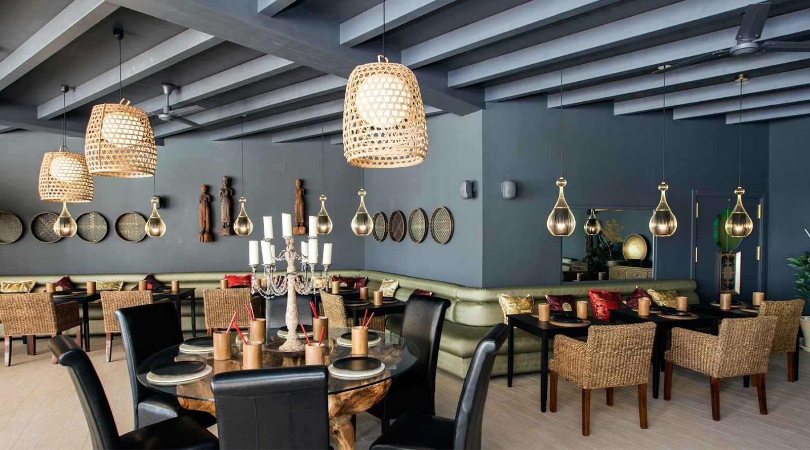 Un comedor moderno con sillas de mimbre, una mesa de vidrio e iluminación colgante.