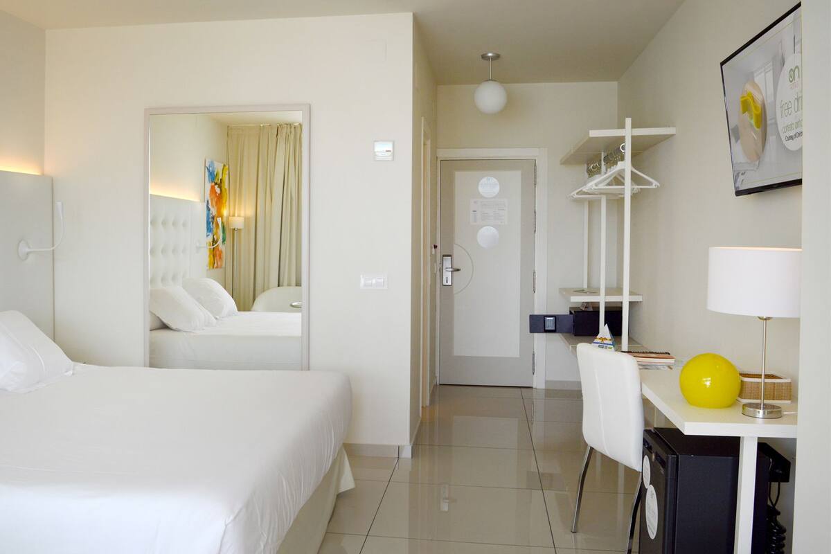A hotel room with a large bed, a desk with a lamp, and a mirror.
