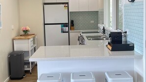 Moderni keittiö, jossa on valkoiset kaapit, keskellä oleva saareke jakkaroineen, jääkaappi ja seinällä oleva kello.
