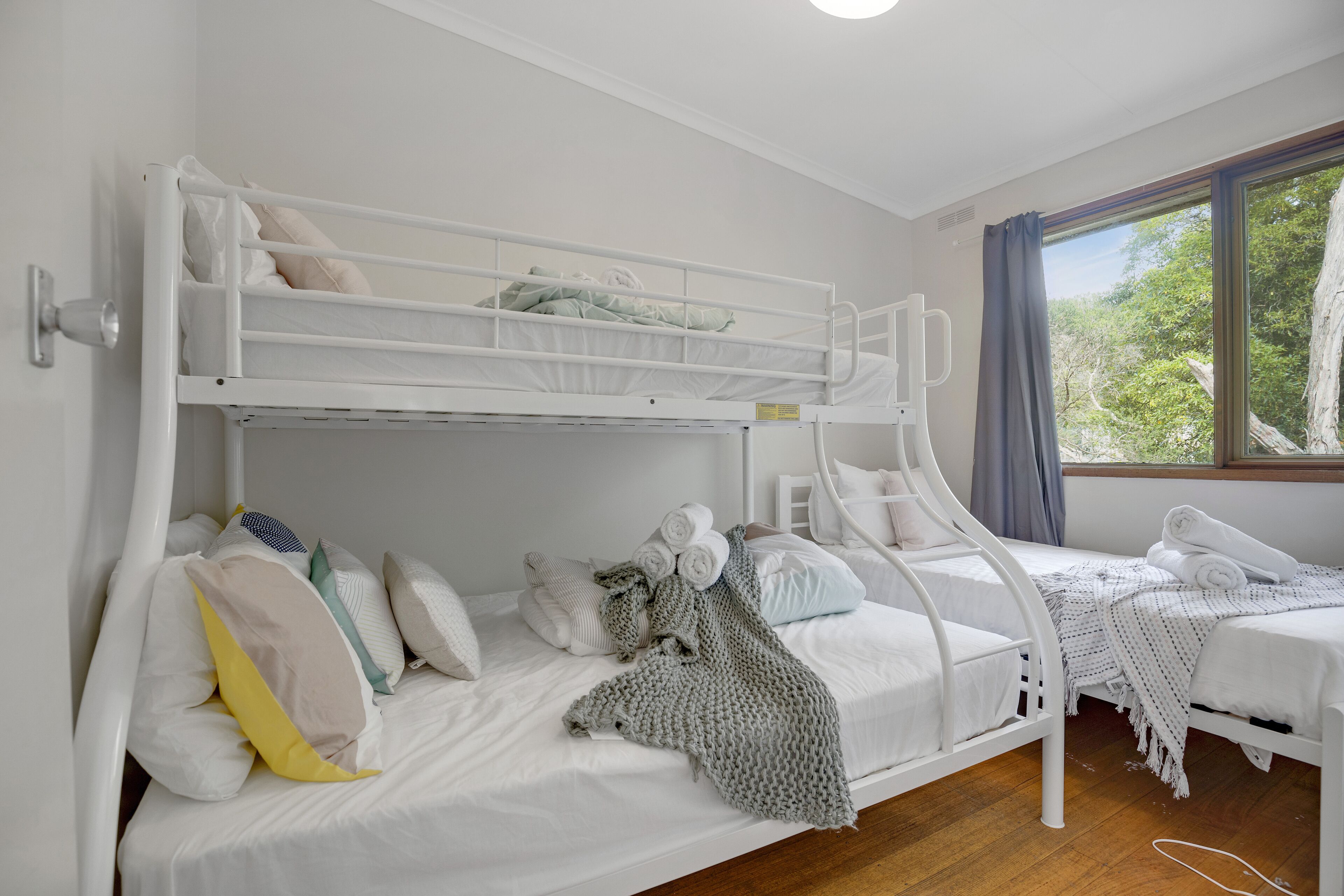 A bunk bed room with a window, white bedding, and a knitted blanket.
