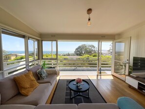 Ein modernes Wohnzimmer mit Sofa, Couchtisch und TV-Möbel. Große Fenster bieten Ausblick ins Freie.
