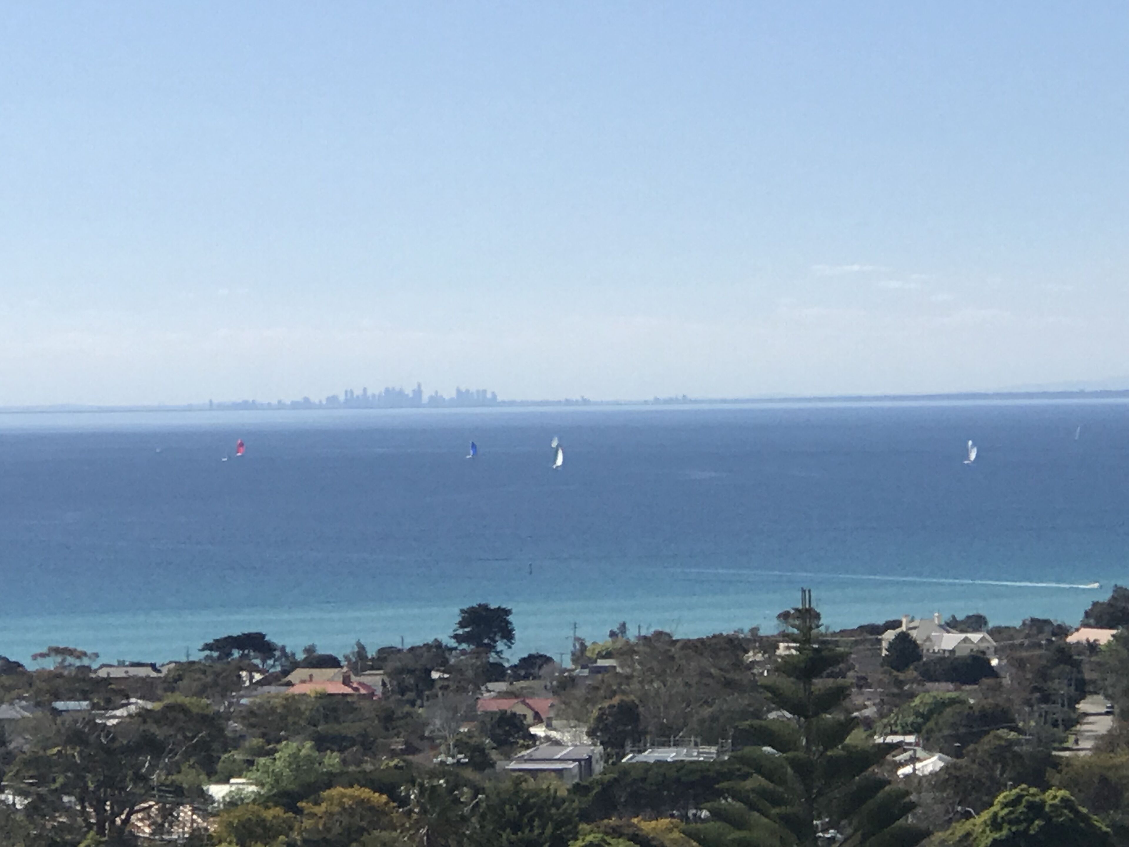 A coastal town with a view of the sea, sailboats, and a distant city skyline.