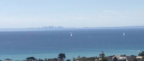 A coastal town with a view of the sea, sailboats, and a distant city skyline.
