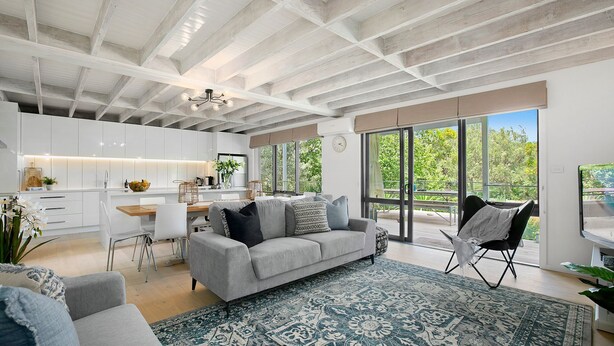 A modern kitchen with white cabinets, a dining area with a gray sofa, and a large window with a view of greenery. - Pet Friendly - Danny Boy Coastal Retreat in Rye (Rye)