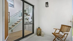 A modern interior with a wooden chair, a lantern, and a staircase leading to a room with a glass door. - Pet Friendly - Danny Boy Coastal Retreat in Rye (Rye)
