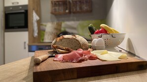 A kitchen counter with a loaf of bread, sliced ham, cheese, and a colander with vegetables and eggs. - Bed 'n Riesling - The vacation apartment in Forst a.d. Wine route with its own garden (Forst an der Weinstraße)