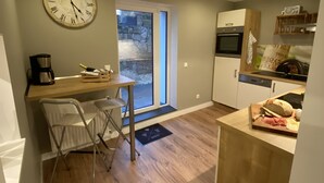 A compact kitchen with a wooden countertop, a dining area with a chair, a clock, and a view through a glass door. - Bed 'n Riesling - The vacation apartment in Forst a.d. Wine route with its own garden (Forst an der Weinstraße)