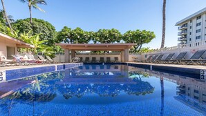 A swimming pool with lounge chairs and a covered seating area, surrounded by palm trees and a building. - KIHEI AKAHI CONDO STEPS FROM BEACH/GARDEN & PEEKABOO OCEAN VIEW/POOL-HOTEL ZONED (Kihei)