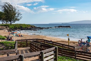 A wooden boardwalk leading to a beach with people relaxing under umbrellas.